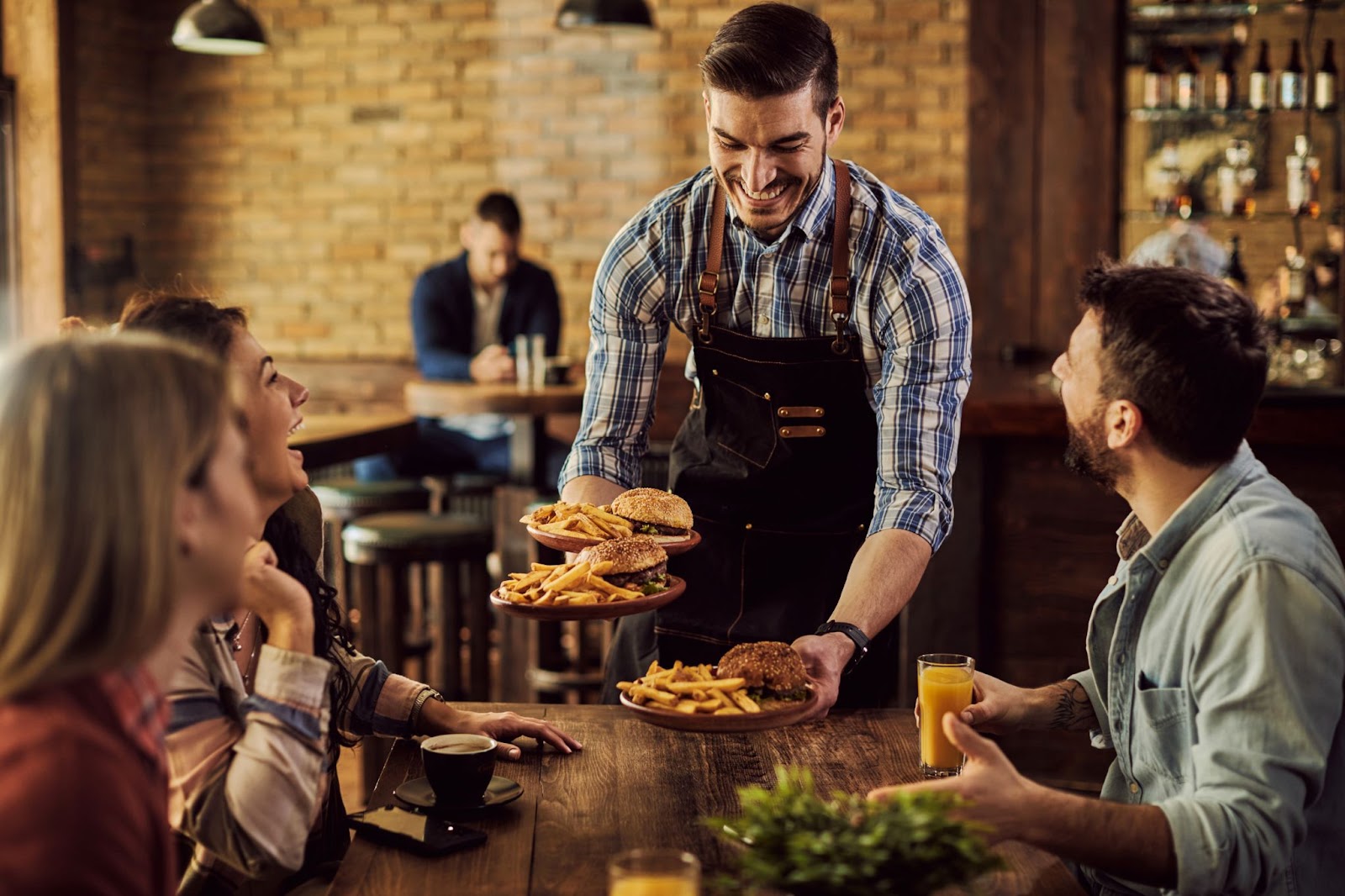 Waiter serving food to group of cheerful friends in a pub