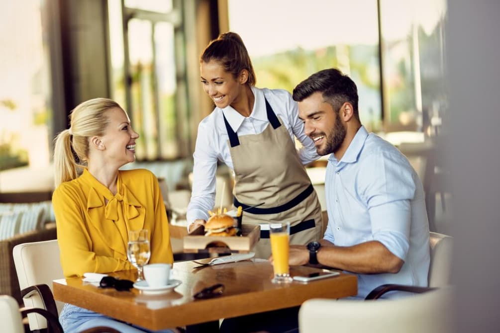 A waitress serving food to a smiling couple at a restaurant
